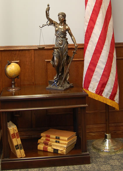 Lady Justice Statue with flag in background and law books in bookcase