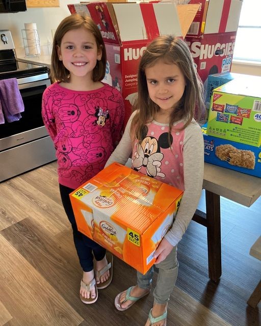 Girls holding box of goldfish in front of table with other donated snacks.